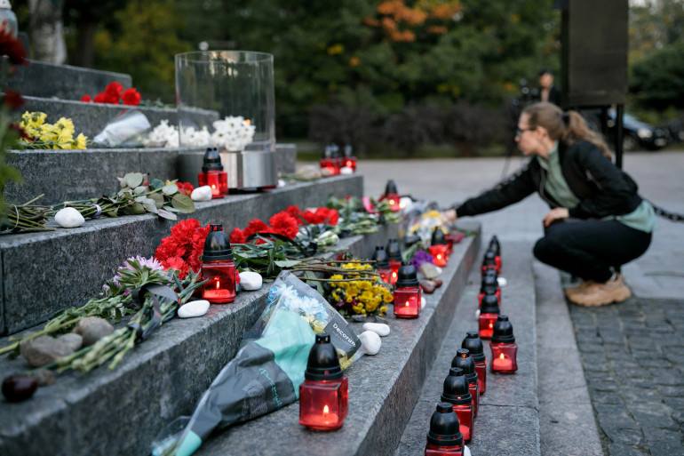 Дівчина кладе пам'ятний символ до Менори. На фото видно сходини у підніжжі пам'ятника, яка встелені лампадками, камінцями та квітами